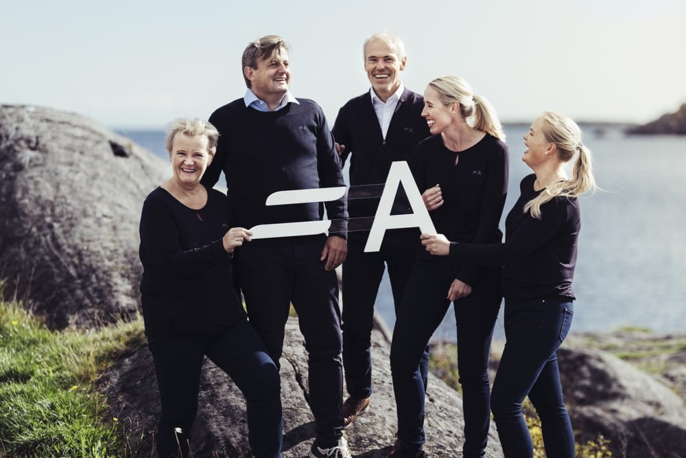 Ansatte i Agder Sparebank står ved havet og holder den nye logoen til banken