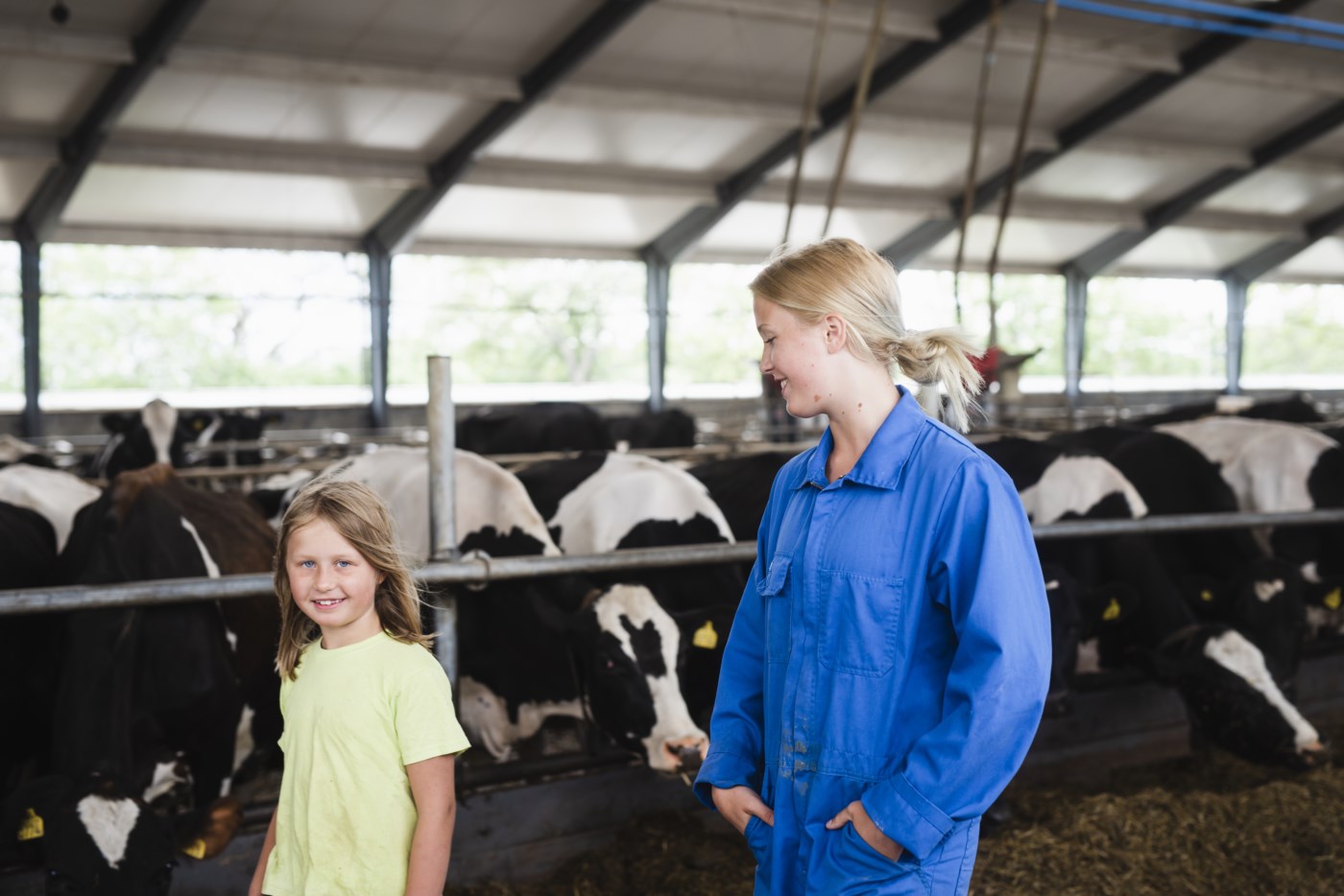 To barn som går i fjøset med kuer i bakgrunnen