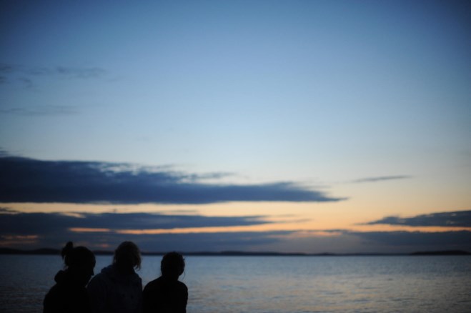 Tre personer ser på solnedgangen over havet. foto